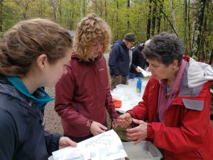 Susan Knight is holding an aquatic plant, showing it to two students during Limno Launch