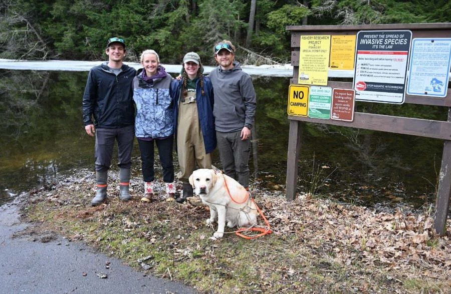 Group of 4 people and one yellow Labrador retriever dog standing on the shore of lake
